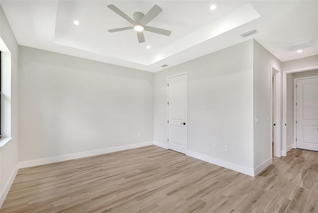 empty room featuring light wood-type flooring, a tray ceiling, and baseboards