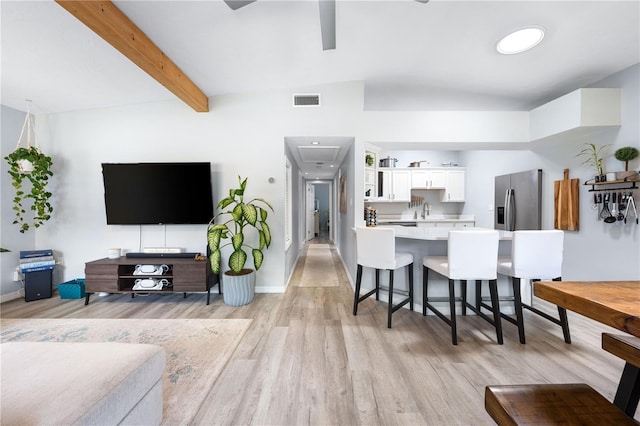 living room with light wood-type flooring, lofted ceiling with beams, and sink