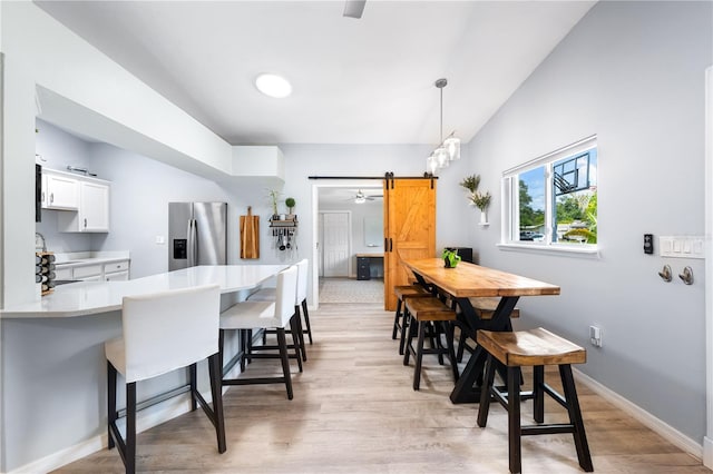 dining area with a barn door, vaulted ceiling, and light hardwood / wood-style floors