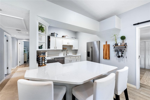 kitchen with a breakfast bar area, stainless steel appliances, kitchen peninsula, white cabinetry, and light wood-type flooring