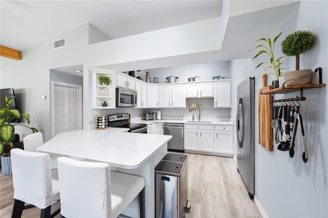 kitchen featuring white cabinets, stainless steel appliances, light hardwood / wood-style floors, kitchen peninsula, and a kitchen breakfast bar