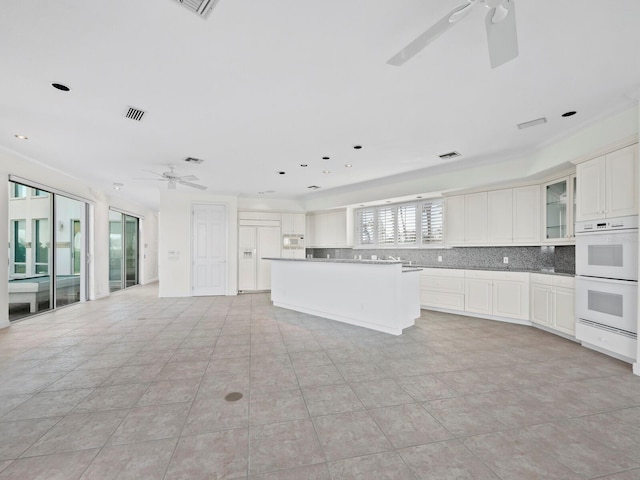 kitchen featuring white cabinetry, backsplash, crown molding, white appliances, and a kitchen island