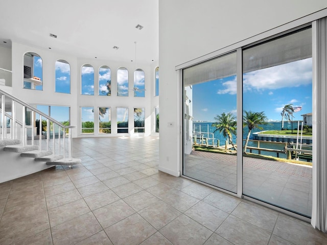 unfurnished living room featuring a water view, light tile patterned floors, and a towering ceiling