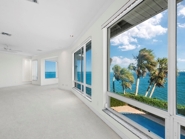 carpeted spare room with a water view, crown molding, ceiling fan, and a healthy amount of sunlight