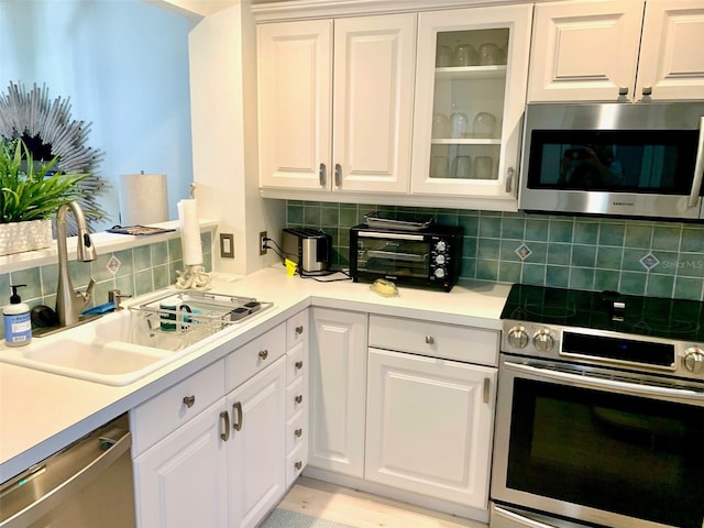 kitchen with stainless steel appliances, decorative backsplash, white cabinetry, and sink