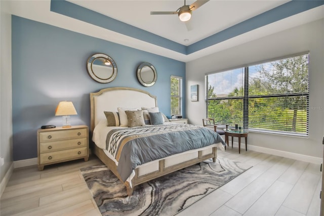 bedroom with a tray ceiling, ceiling fan, and light hardwood / wood-style flooring