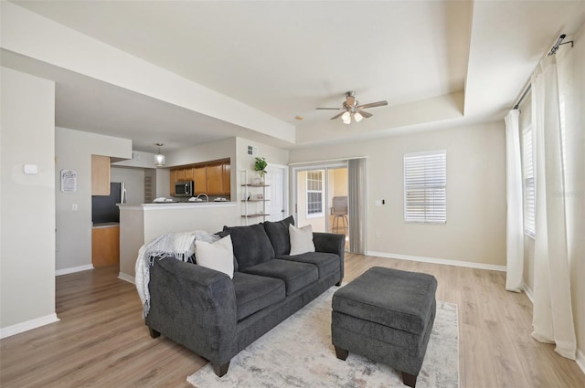 living room with light hardwood / wood-style flooring, a raised ceiling, and ceiling fan