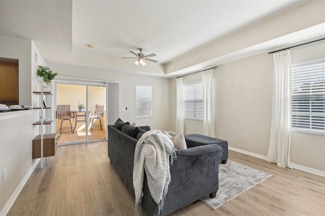 living room with light hardwood / wood-style flooring, ceiling fan, and a tray ceiling