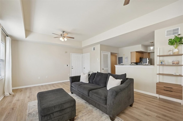 living room featuring a tray ceiling, ceiling fan, and light wood-type flooring