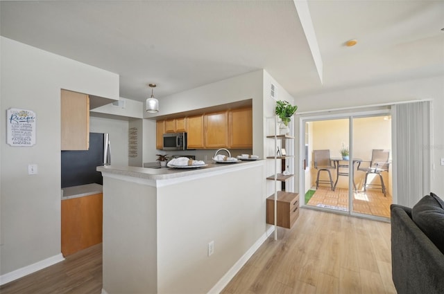 kitchen with hanging light fixtures, appliances with stainless steel finishes, kitchen peninsula, and light hardwood / wood-style flooring