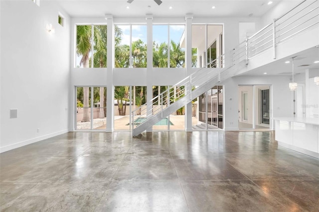 unfurnished living room featuring concrete flooring, a towering ceiling, ceiling fan, and a healthy amount of sunlight