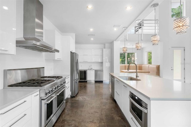 kitchen with sink, a center island with sink, wall chimney range hood, white cabinetry, and appliances with stainless steel finishes