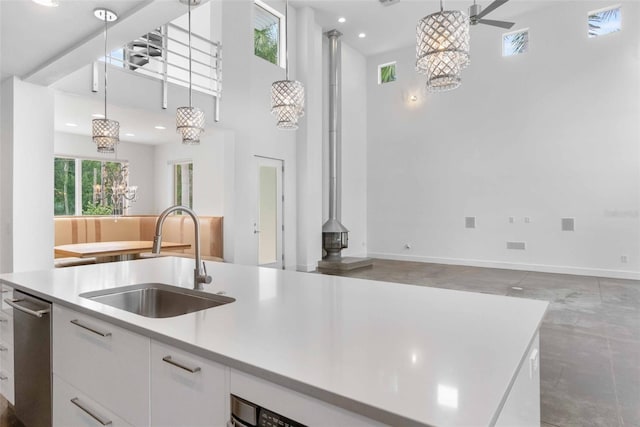 kitchen featuring hanging light fixtures, a towering ceiling, white cabinets, a center island with sink, and sink