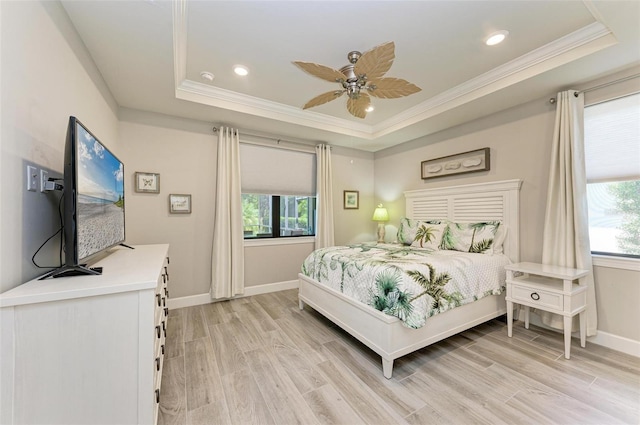 bedroom featuring ceiling fan, ornamental molding, a tray ceiling, and light wood-type flooring