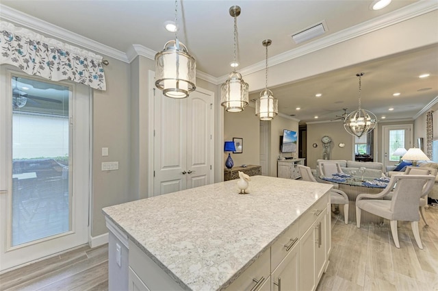 kitchen with white cabinetry, a center island, hanging light fixtures, light hardwood / wood-style flooring, and ornamental molding