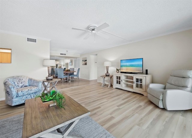 living room featuring ornamental molding, a textured ceiling, light hardwood / wood-style flooring, and ceiling fan