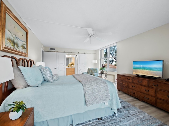 bedroom with light wood-type flooring, connected bathroom, ceiling fan, and a barn door