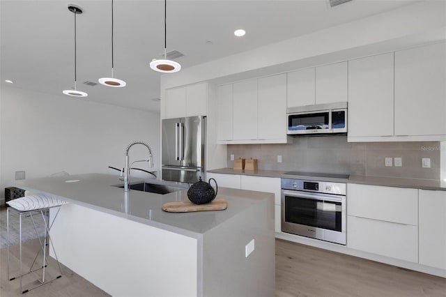 kitchen with light hardwood / wood-style floors, sink, tasteful backsplash, appliances with stainless steel finishes, and decorative light fixtures