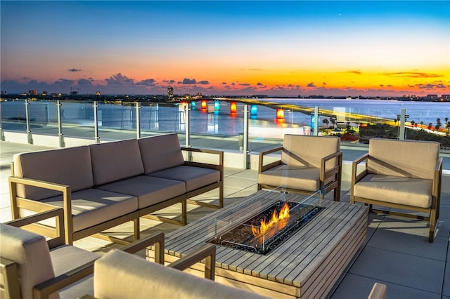 balcony at dusk featuring an outdoor living space with a fire pit and a water view