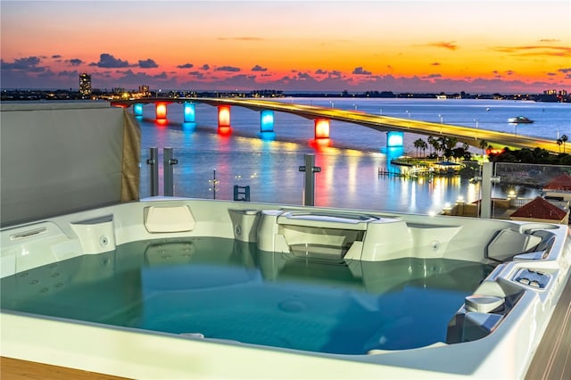 pool at dusk featuring a hot tub and a water view