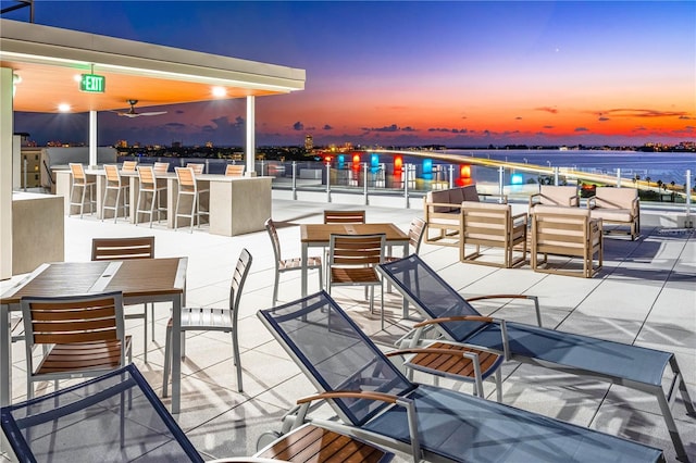 patio terrace at dusk featuring a water view and a bar