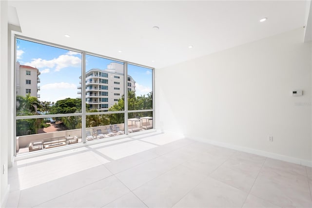 unfurnished room with light tile patterned flooring and a wall of windows