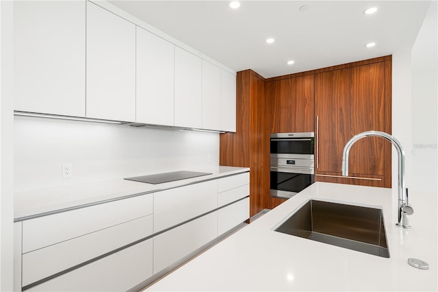 kitchen featuring black electric cooktop, sink, multiple ovens, and white cabinets