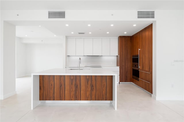 kitchen with sink, decorative backsplash, an island with sink, and white cabinets