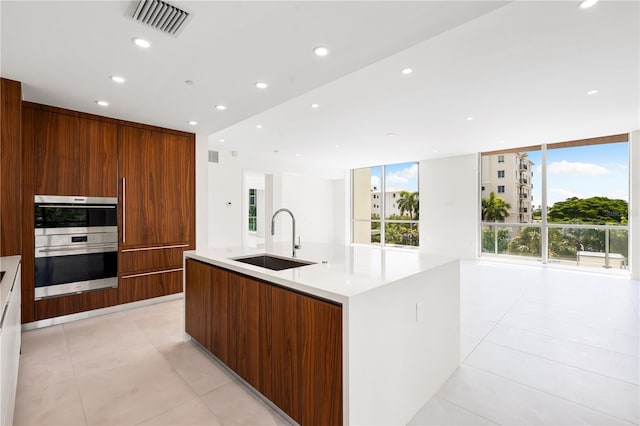 kitchen with light tile patterned flooring, floor to ceiling windows, sink, double oven, and a large island