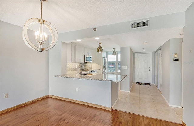 kitchen featuring kitchen peninsula, appliances with stainless steel finishes, white cabinetry, and pendant lighting