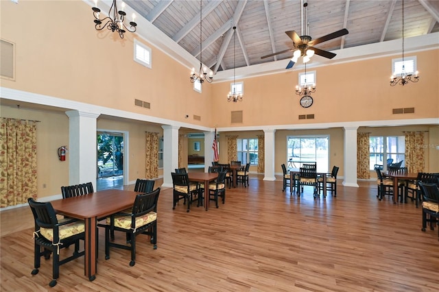 dining area featuring ceiling fan with notable chandelier, a towering ceiling, light hardwood / wood-style floors, and decorative columns