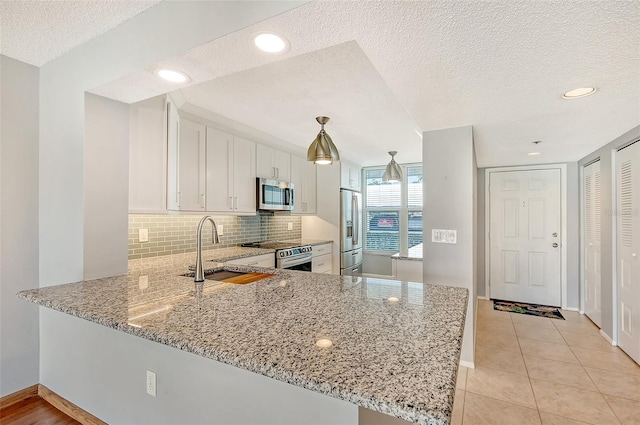 kitchen with kitchen peninsula, stainless steel appliances, sink, white cabinetry, and hanging light fixtures