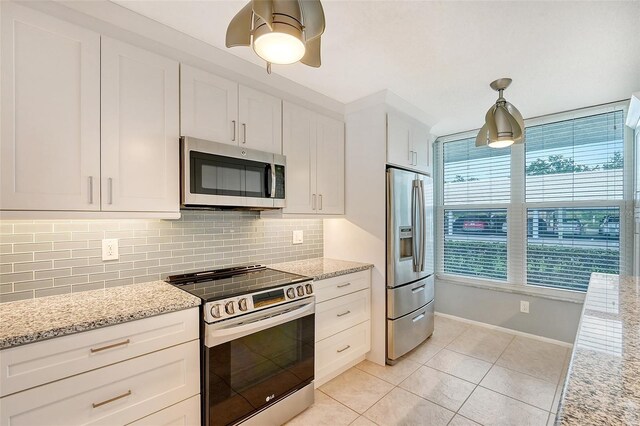 kitchen featuring light stone countertops, white cabinetry, stainless steel appliances, pendant lighting, and light tile patterned flooring