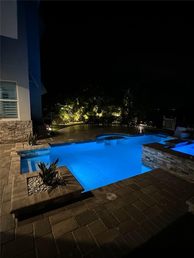 pool at twilight featuring a hot tub and a patio