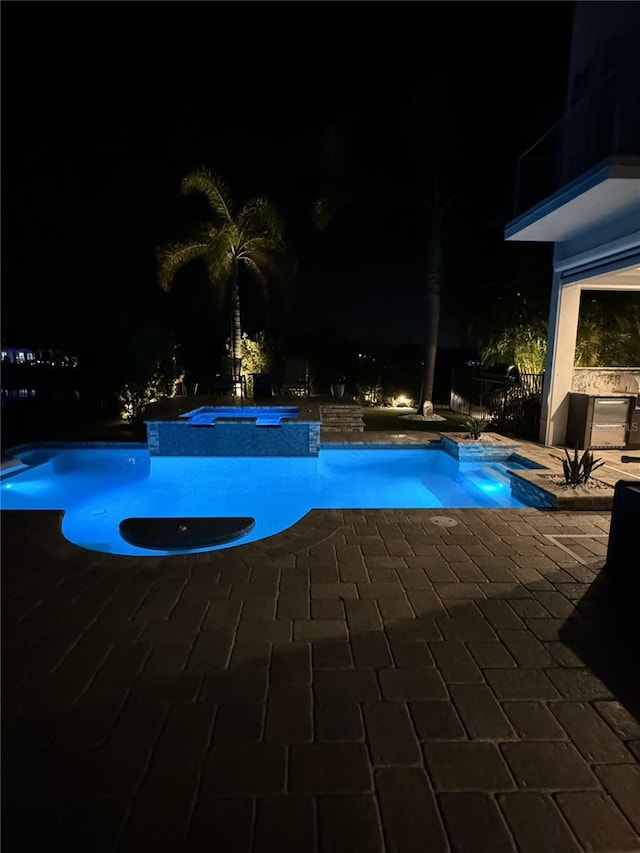 pool at twilight featuring an in ground hot tub and a patio