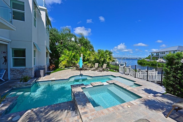 view of swimming pool featuring an in ground hot tub, a water view, and a patio area