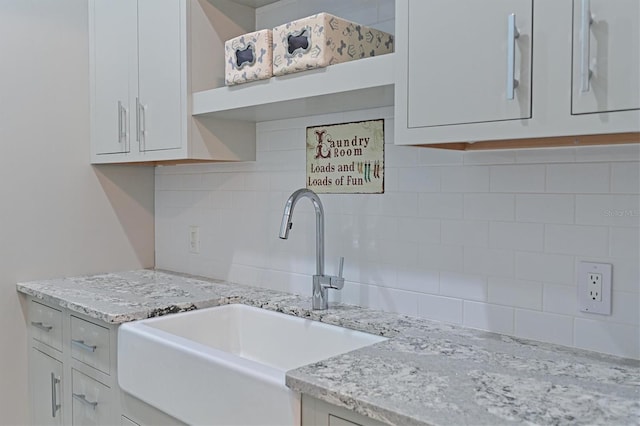 kitchen with white cabinetry, sink, decorative backsplash, and light stone countertops