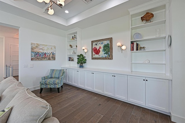 living area with built in shelves, dark hardwood / wood-style floors, and a tray ceiling