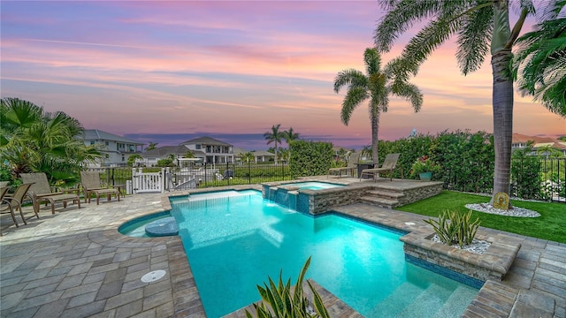 pool at dusk featuring a patio area and an in ground hot tub