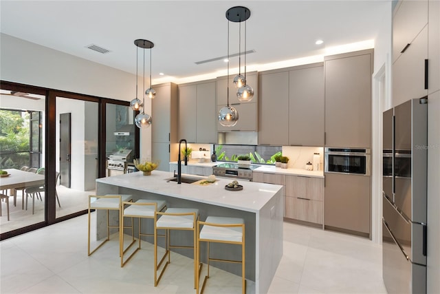 kitchen featuring gray cabinetry, a kitchen breakfast bar, an island with sink, pendant lighting, and appliances with stainless steel finishes