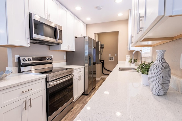 kitchen with light stone counters, sink, white cabinetry, stainless steel appliances, and light hardwood / wood-style floors