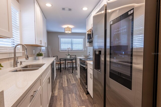 kitchen with sink, white cabinetry, stainless steel appliances, light stone countertops, and dark hardwood / wood-style flooring