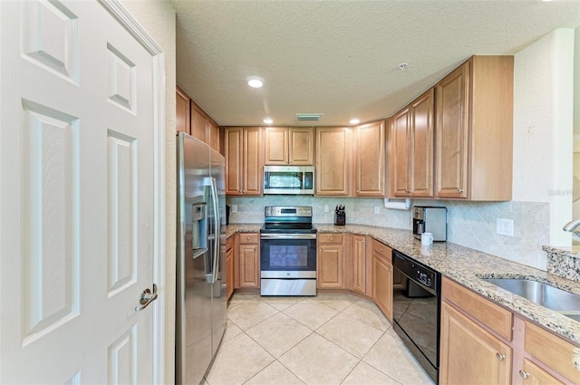 kitchen with light tile patterned floors, light stone countertops, stainless steel appliances, sink, and a textured ceiling