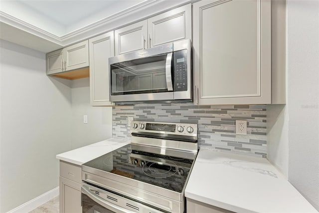 kitchen with stainless steel appliances, gray cabinetry, light stone countertops, and decorative backsplash