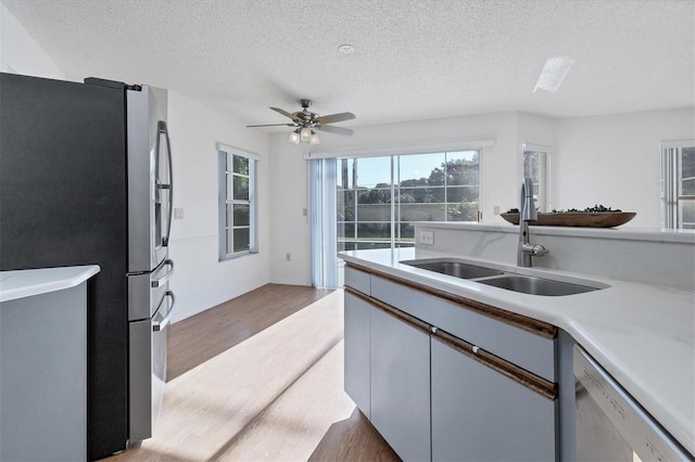 kitchen with light countertops, appliances with stainless steel finishes, a sink, a textured ceiling, and wood finished floors