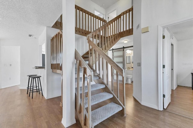 stairway with a barn door, baseboards, visible vents, wood finished floors, and a textured ceiling