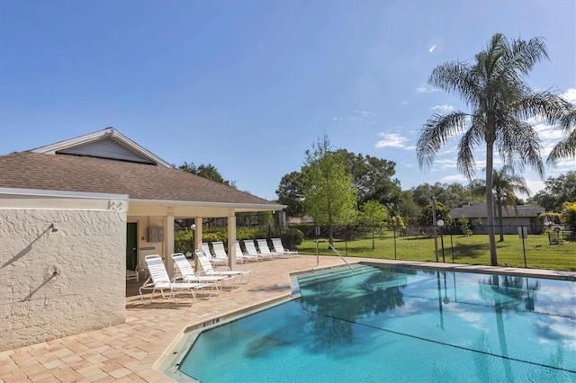 community pool with a patio, a lawn, and fence