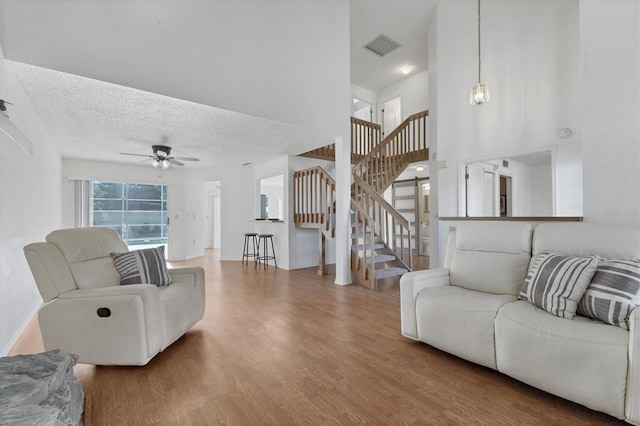 living area featuring visible vents, a ceiling fan, a textured ceiling, wood finished floors, and stairs