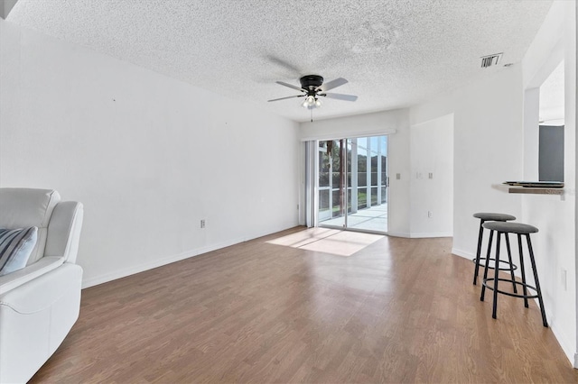 living area featuring a textured ceiling, wood finished floors, a ceiling fan, and baseboards