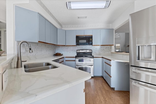 kitchen with a sink, light wood-style floors, blue cabinetry, appliances with stainless steel finishes, and tasteful backsplash